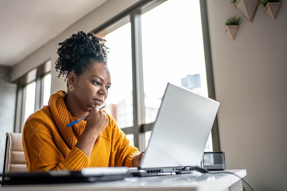 A woman in a yellow sweater concentrating on her laptop, symbolizing intelligence, focus, and the effort to challenge myths about ADHD and IQ.