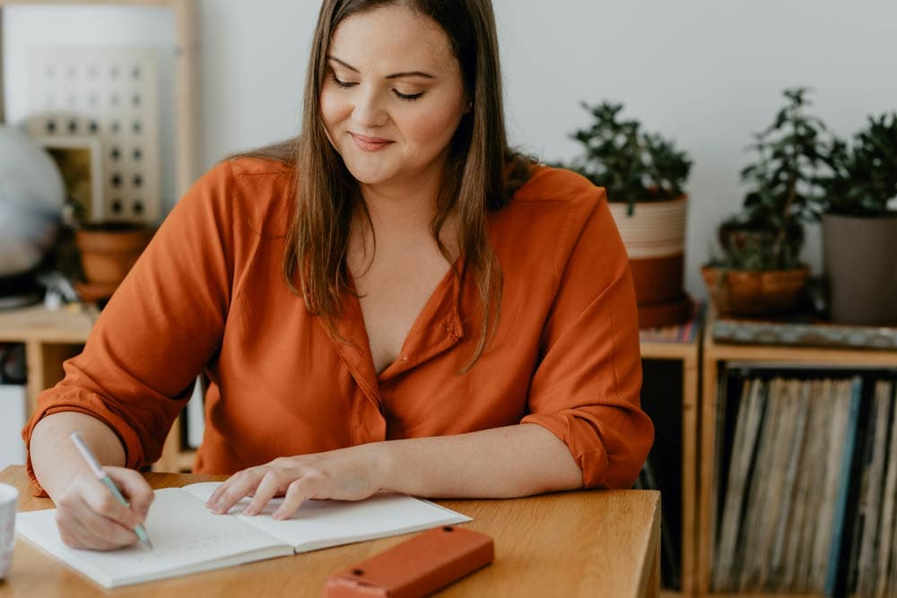A woman writing in a journal at home, representing how journaling supports emotional regulation and clarity for individuals with ADHD.