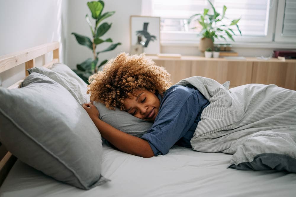 A woman peacefully sleeping in bed, representing the importance of restful nights and better focus for people with ADHD.