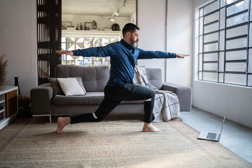 A man practicing yoga at home while following an online workout, illustrating ADHD-friendly fitness approaches that promote focus, balance, and routine flexibility.