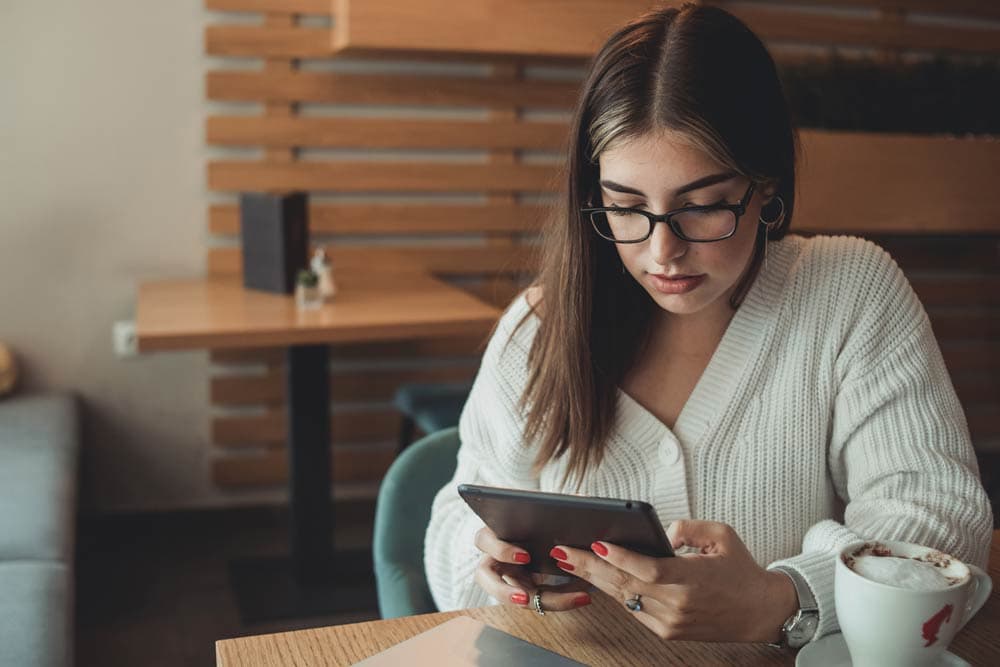 Woman reading on a tablet in a café with a coffee cup nearby, representing adult ADHD education and self-learning.