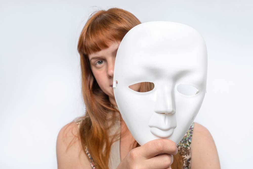 A woman holding a white mask in front of her face, symbolizing how coexisting mental health conditions can hide or mask the symptoms of ADHD in adults.