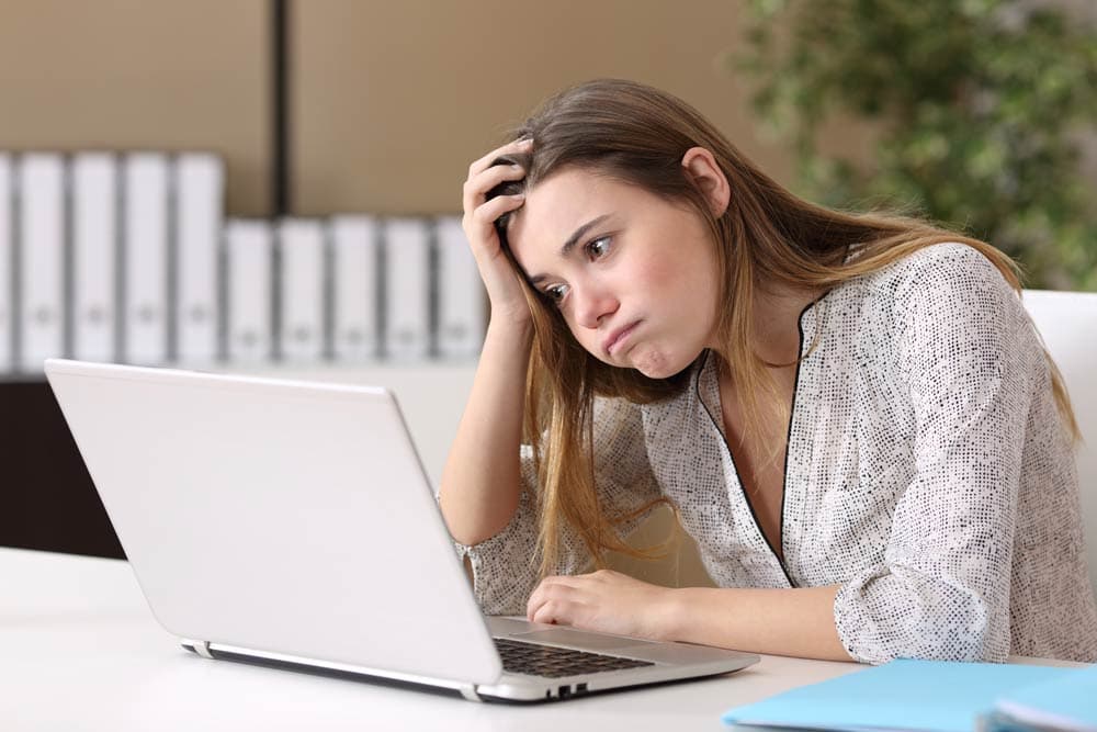 A frustrated teenage girl sits in front of her laptop with her head in her hand, illustrating the emotional challenges of frustration and anger management in teens with ADHD.