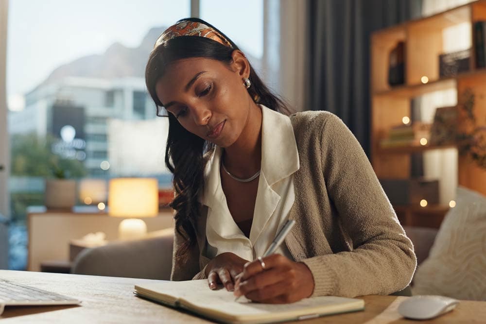 Woman writing in a journal at her desk, creating a structured ADHD-friendly daily routine for better focus and stress management.
