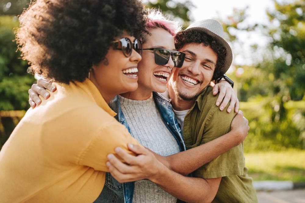 Three friends laughing and hugging outdoors, representing the importance of supportive communities and friendships for individuals with ADHD.