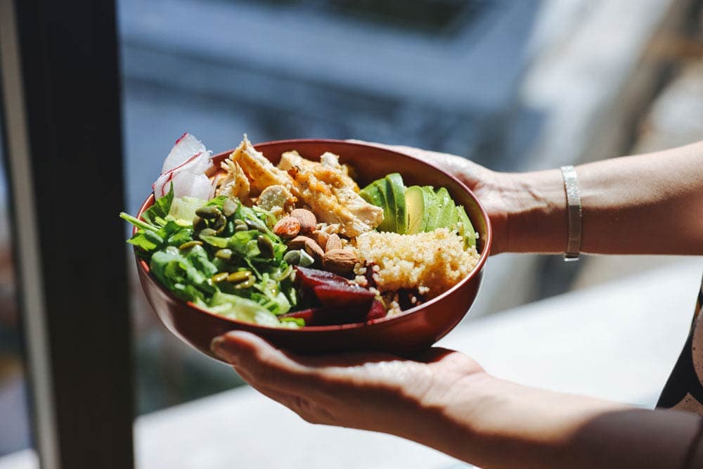 Bowl of healthy food with chicken, quinoa, avocado, greens, nuts, and seeds, representing foods that support focus and memory in individuals with ADHD.