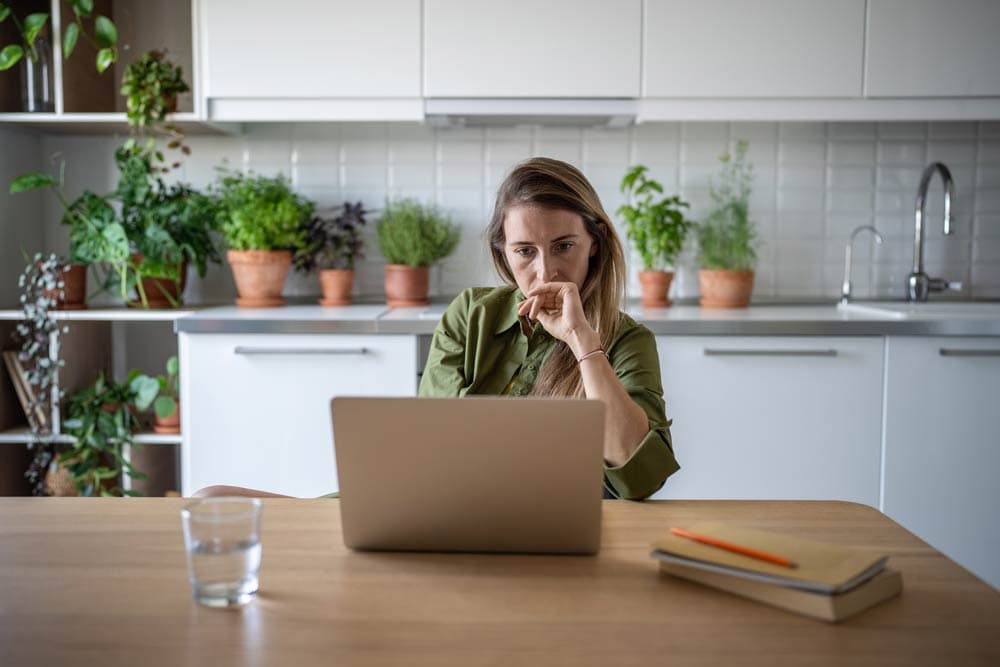Woman working on a laptop at a kitchen table, representing the challenges of career planning with ADHD.