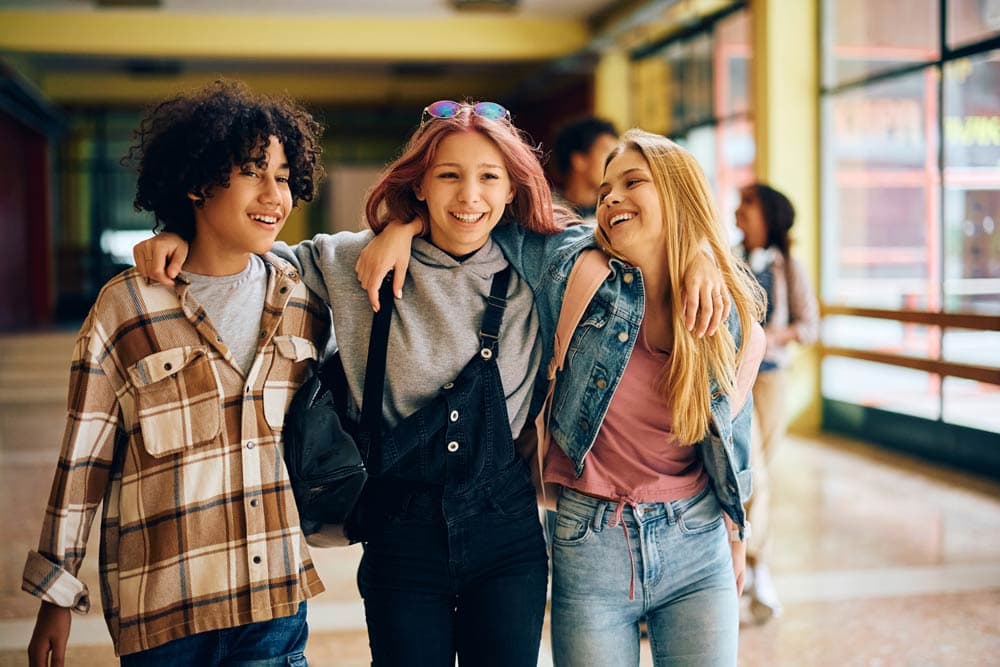 Three teenagers walk together smiling with arms around each other, symbolizing how teens with ADHD can build supportive friendships and lasting social connections.