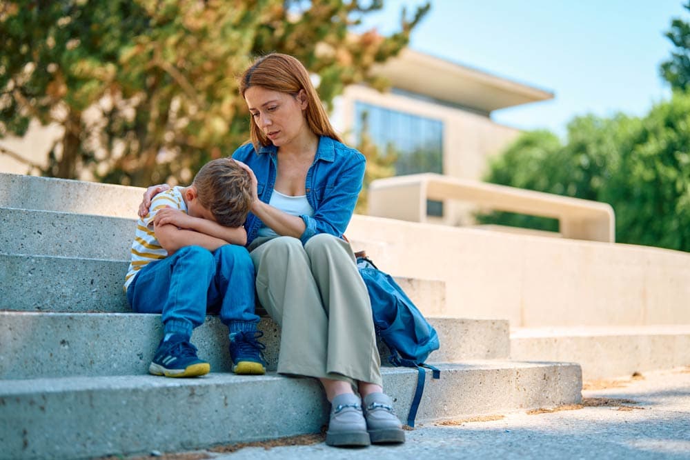 A mother comforts her upset young son sitting on outdoor steps, illustrating ADHD meltdown management with empathy, structure, and parental support.