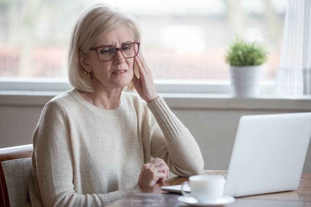 Older woman with ADHD sitting at a laptop, appearing thoughtful and experiencing memory challenges related to aging and attention difficulties.