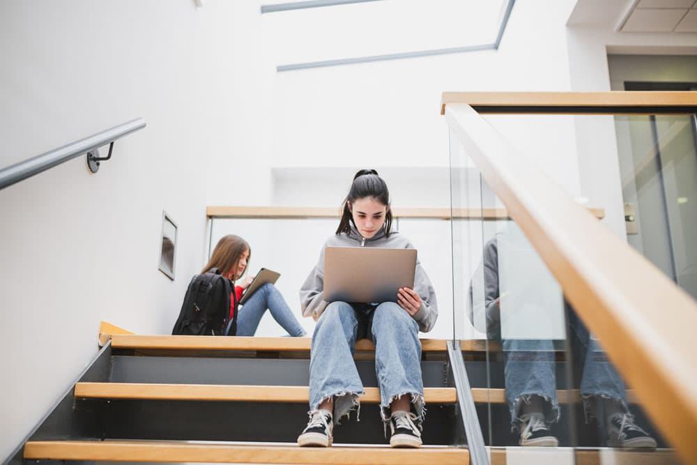 A teen sitting on school stairs working on a laptop, symbolizing the transition from high school to post-secondary education or vocational paths with ADHD.