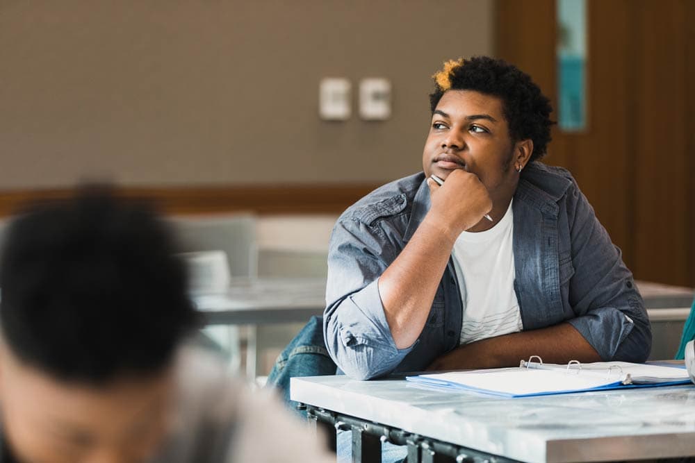 Teen student sitting at a desk and looking thoughtful, representing self-identity and self-esteem challenges in ADHD.