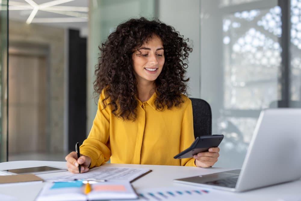 A young professional with ADHD smiling while working at a desk with a laptop and planner, symbolizing the transition from student to employee and strategies for workplace success.