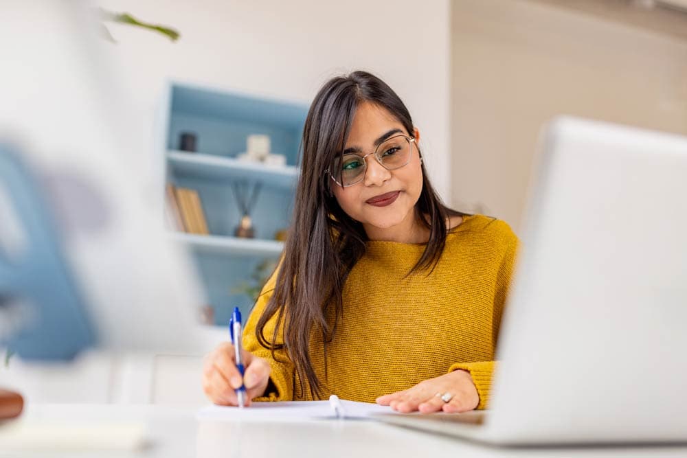Woman writing notes while studying at a desk, representing learning about ADHD symptoms and management strategies.