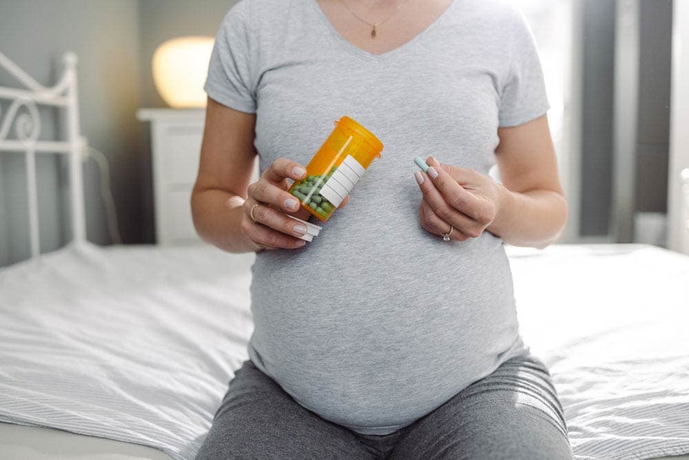 Pregnant woman holding prescription bottle and ADHD medication pills while sitting on a bed, highlighting treatment decisions during pregnancy.