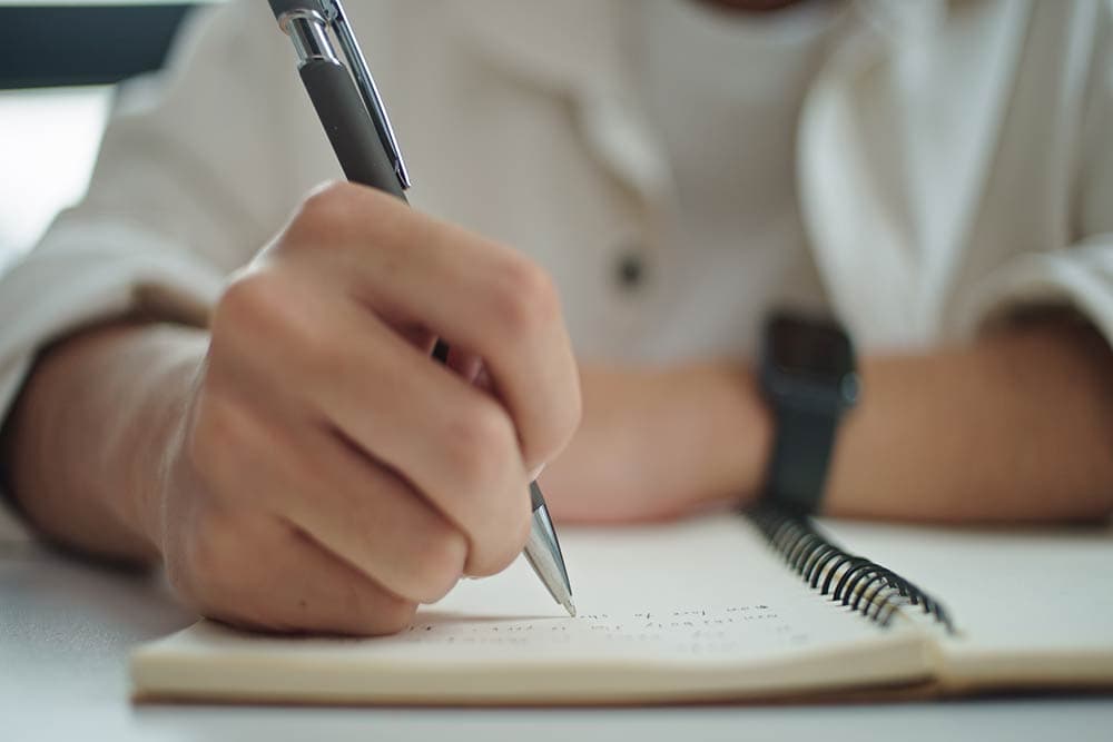 Close-up of a student writing notes in a spiral notebook, representing academic note-taking support for college and university students with ADHD.