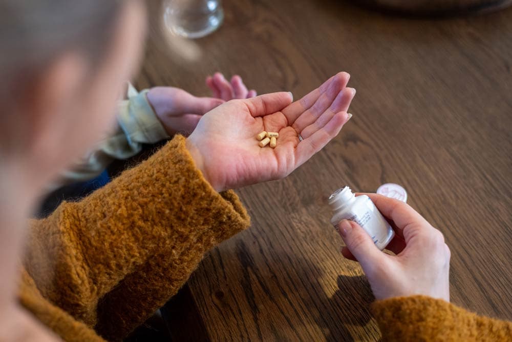 A parent holds ADHD medication capsules in their hand while sitting at a table, symbolizing the decision-making process of when to consider medication for children with ADHD.