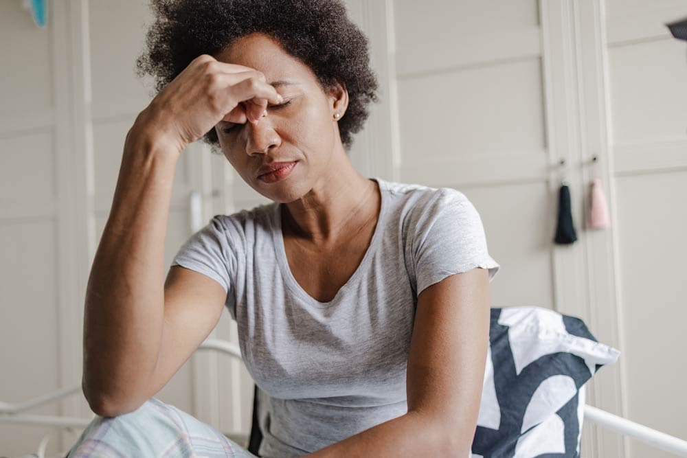 A woman sitting with her hand on her forehead looking stressed, representing the challenges of emotional dysregulation often experienced by individuals with ADHD.