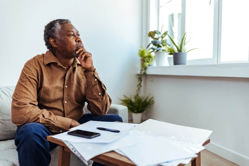 An older man sitting thoughtfully with papers and a phone, representing the struggles adults face when ADHD goes undiagnosed.