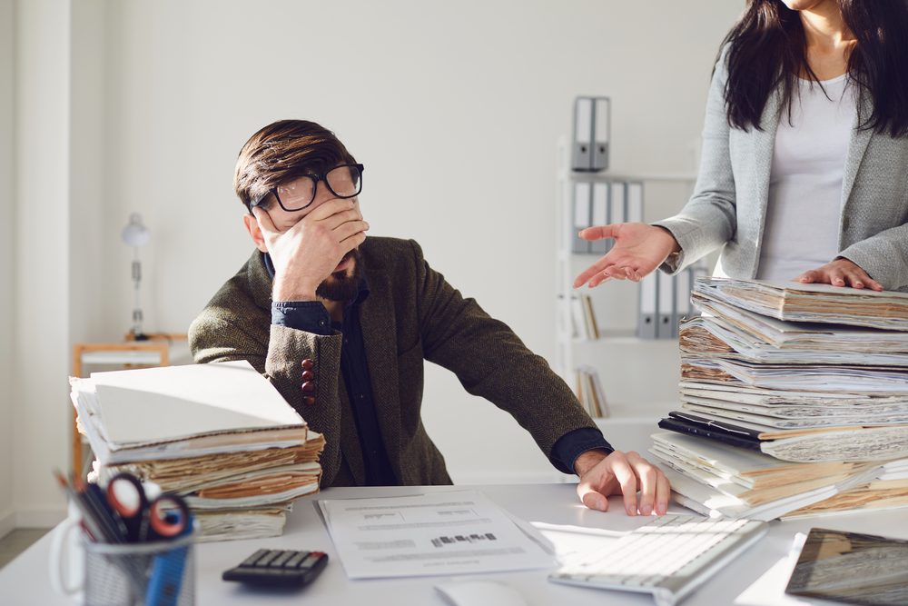 Person at an office desk mid-afternoon rubbing their eyes beside a cold cup of coffee