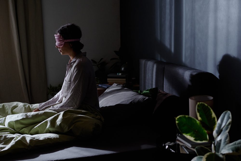 Woman sitting on her bed with a laptop closed, looking down at her hands