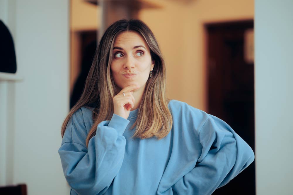 A thoughtful woman looking upward with a hand on her chin, representing the challenges of working memory and forgetfulness in ADHD.