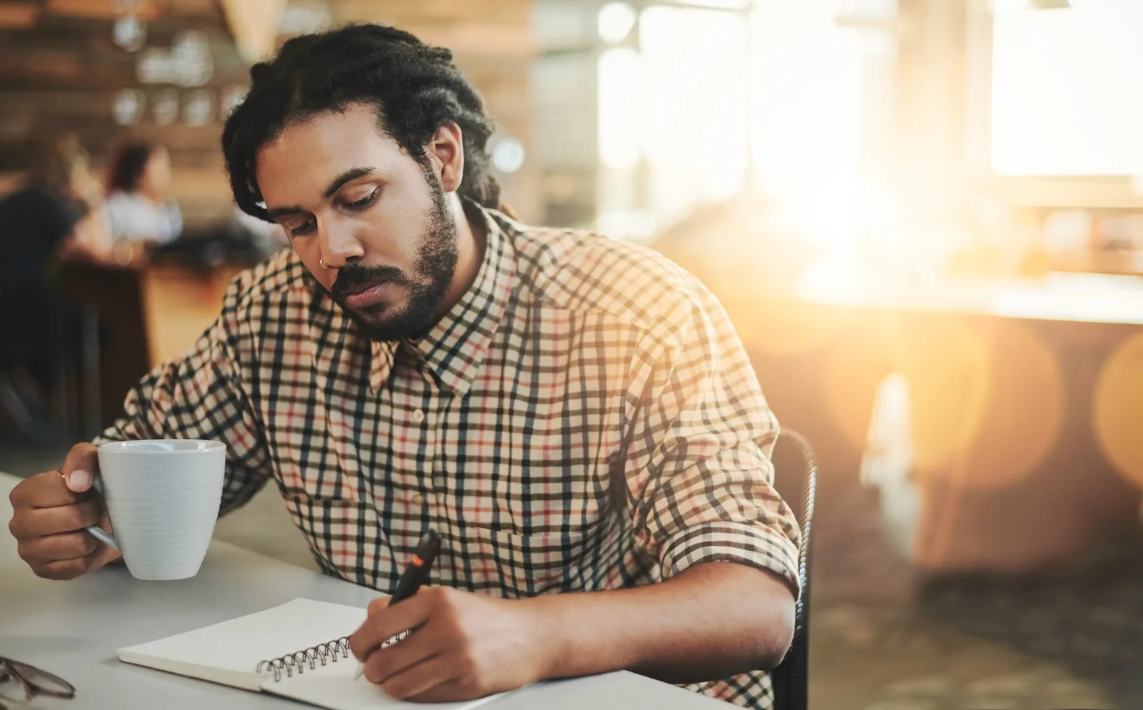 Man writing notes in a journal at a sunny public library table, using free community resources to manage ADHD on a budget.