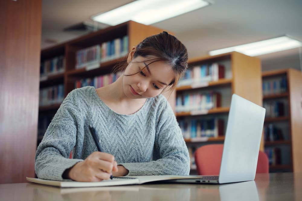 A student studying with a laptop and notebook in a library, representing ADHD-friendly digital tools and apps that support focus, time management, and learning.