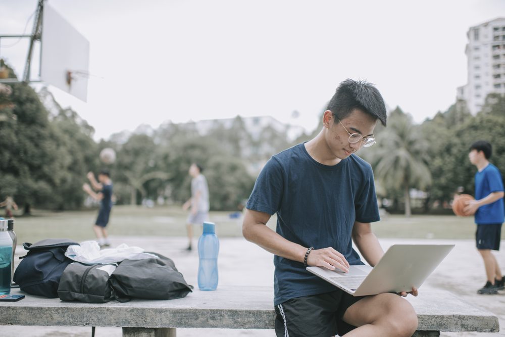 Teenager at a kitchen table writing in a paper agenda next to a phone