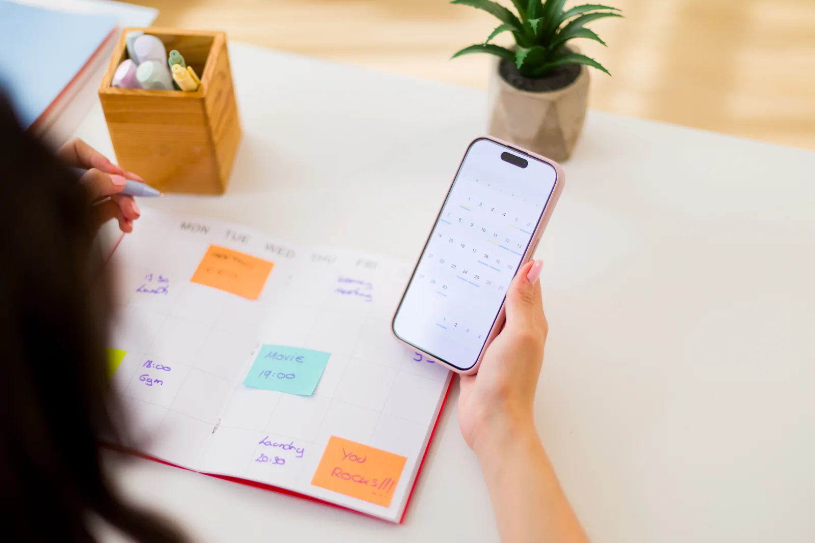 Woman checking her calendar and smartphone at a bright kitchen counter, planning upcoming appointments.