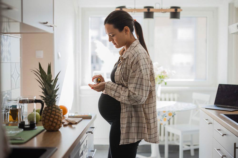 Pregnant woman in kitchen holding medication bottle and pills, reflecting decisions about ADHD medication use during pregnancy and child health outcomes.