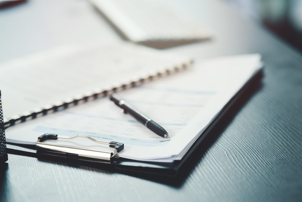 Paperback book open on a desk beside a habit tracker grid and a pencil