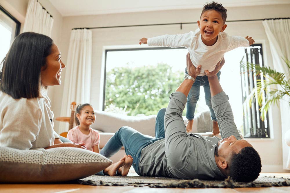 A happy family playing together at home, with a parent lifting a child in the air, symbolizing balance, joy, and connection while parenting with ADHD.