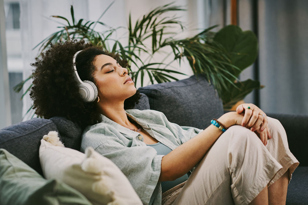 A student with ADHD relaxing on a couch while listening to music with headphones, illustrating the importance of self-care routines for mental health in college.