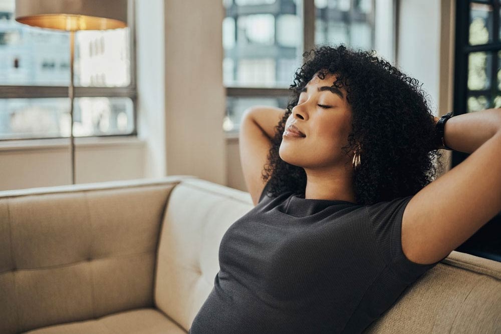 A relaxed student with ADHD leaning back on a couch with eyes closed, showing the importance of building daily rest routines to support mental health and prevent burnout.
