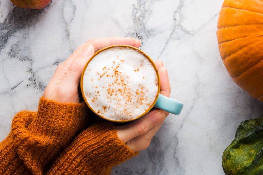 Hands holding a ceramic mug of black coffee on a wooden table