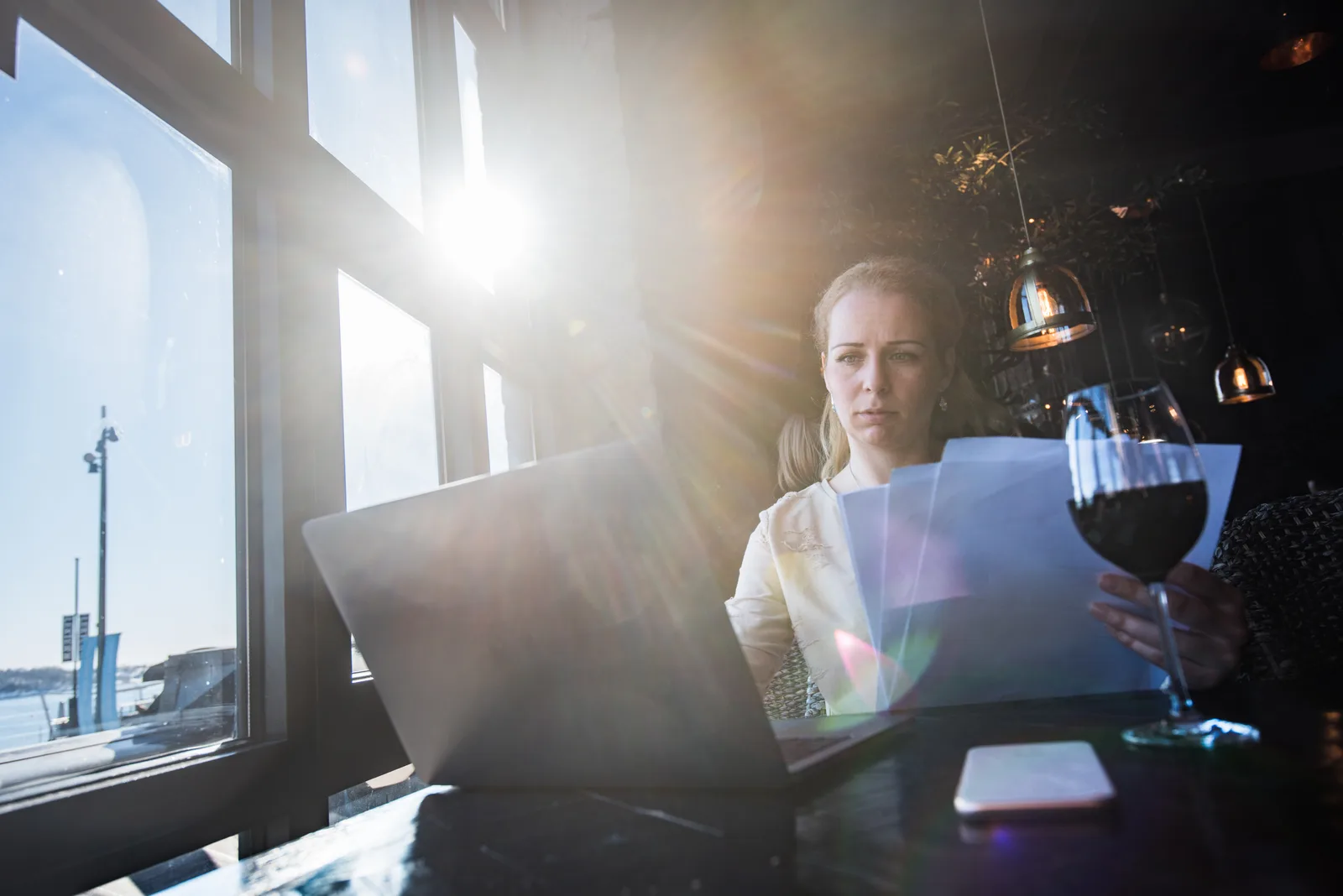 A woman highlighting sections of her printed benefits booklet at a sunlit dining table, with a laptop open beside her.