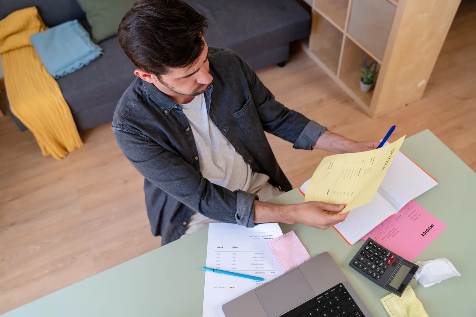 A man organizing a year of medical receipts into labelled folders beside a calculator in a cozy home office.