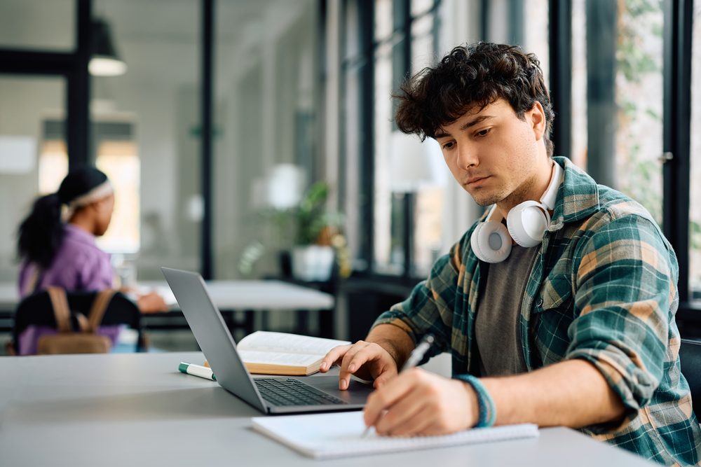 Student at a laptop reviewing a spreadsheet of job applications in a campus lounge
