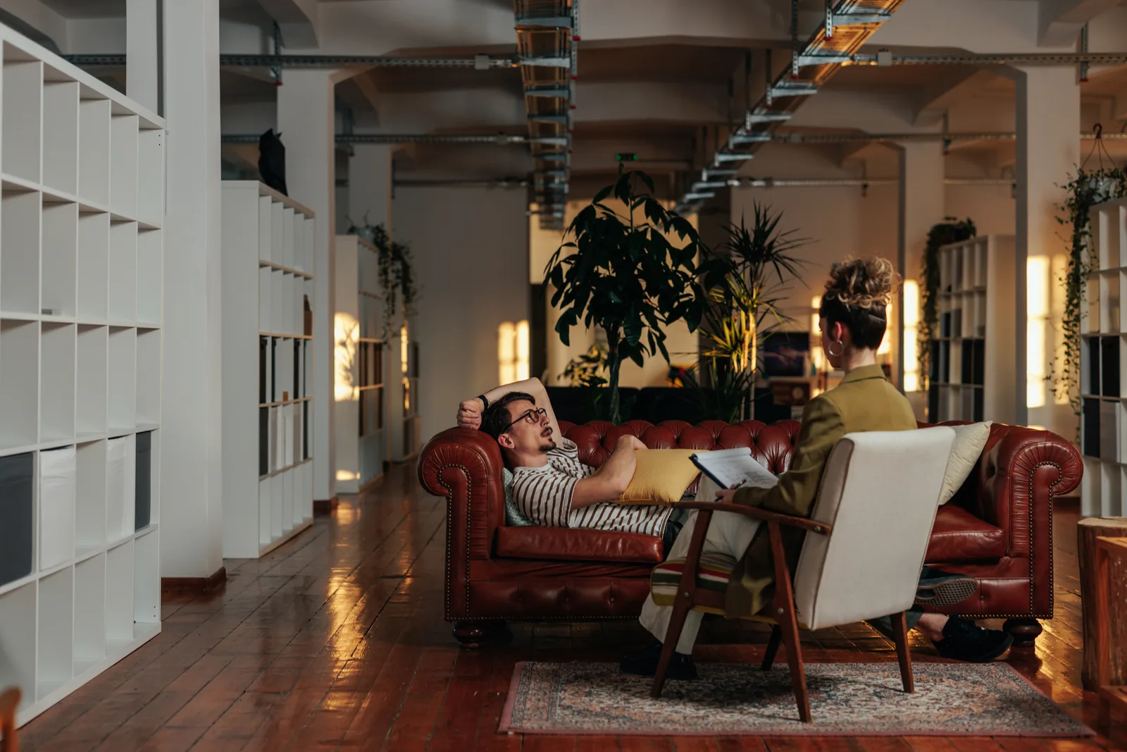 Two people in armchairs having a calm, focused conversation in a warmly lit counselling office.