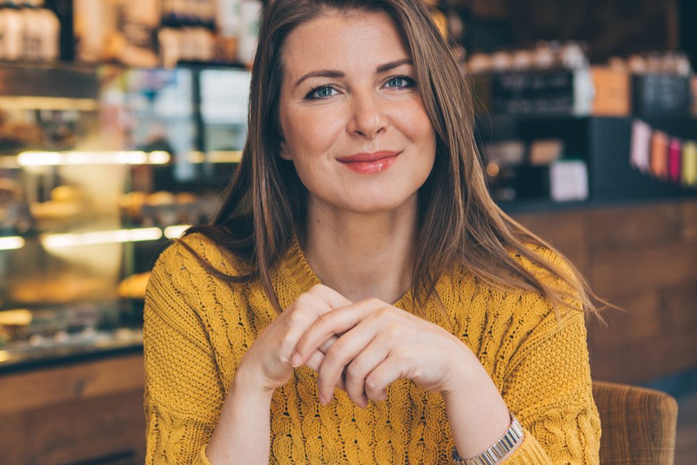 Woman at a café window seat checking her phone, second coffee untouched across the table