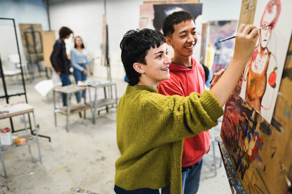 Two teens smiling while painting together in an art class, representing how hobbies and passions help ADHD teens build confidence and identity.