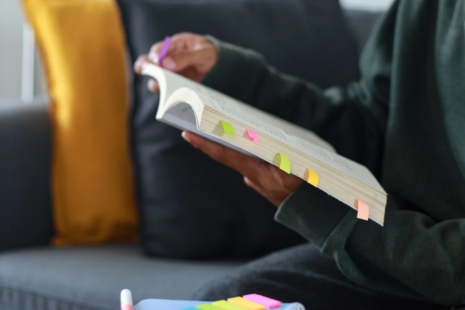 A person sits in a cozy armchair reading a thick reference book with sticky notes marking pages, making sense of diagnostic criteria in plain language.