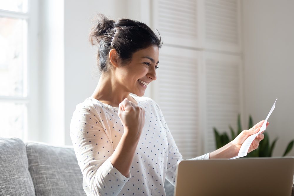 Person at a kitchen table reading a government letter beside a laptop and a folder