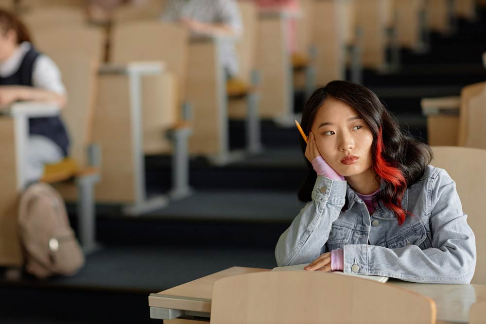 Student sitting in a lecture hall looking distracted, symbolizing executive function challenges with ADHD such as focus and organization difficulties.