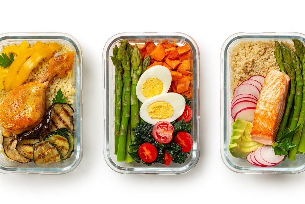 Packed lunch containers lined up on a counter beside a phone showing an alarm