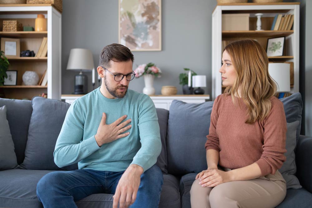 Man and woman having a calm conversation on a couch, representing constructive communication about ADHD-related challenges.