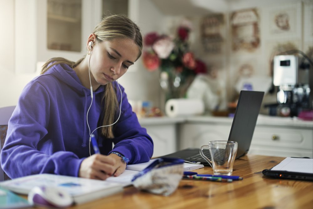 Teenage girl with head in hands at a desk while a parent stands in the doorway