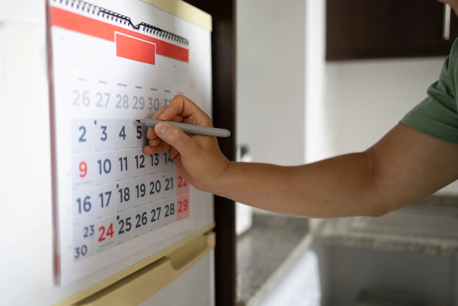 Man marking a renewal date on a wall calendar in his kitchen, staying ahead of his ADHD prescription refill schedule.