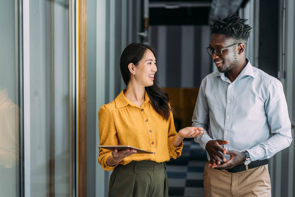A woman and man talking and smiling in a hallway, representing collaboration and awareness in addressing gender bias in ADHD diagnosis and treatment.